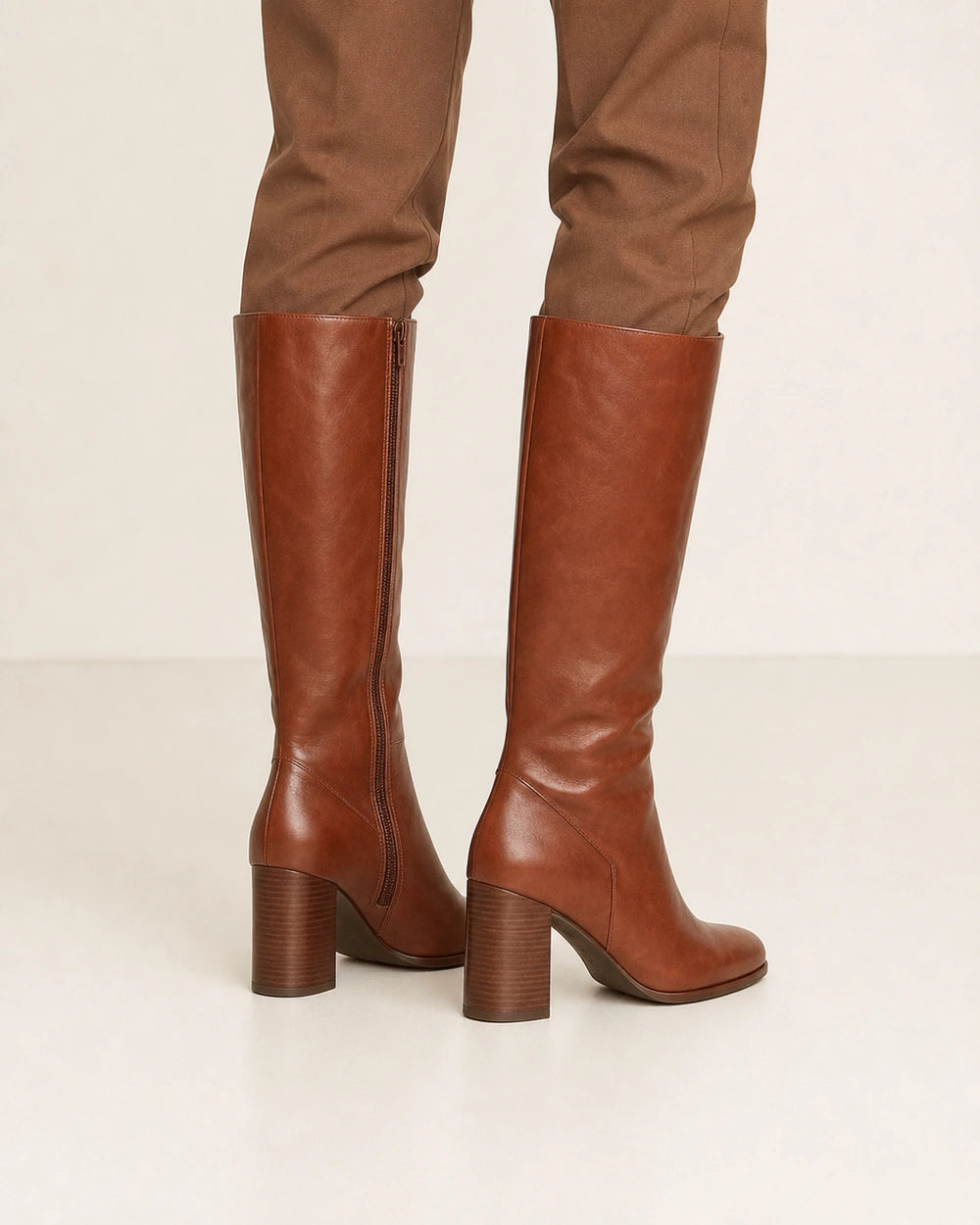 Women's cognac-brown knee-high boots with a sculpted block heel, rear three-quarter view.